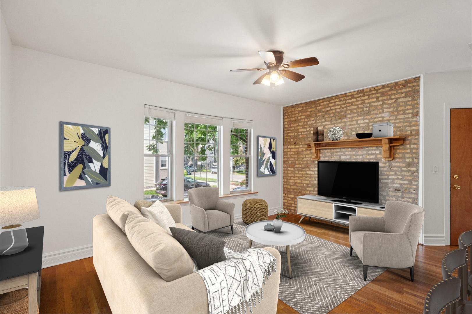 Staged living room with exposed brick television wall, hardwood floors, and large windows.