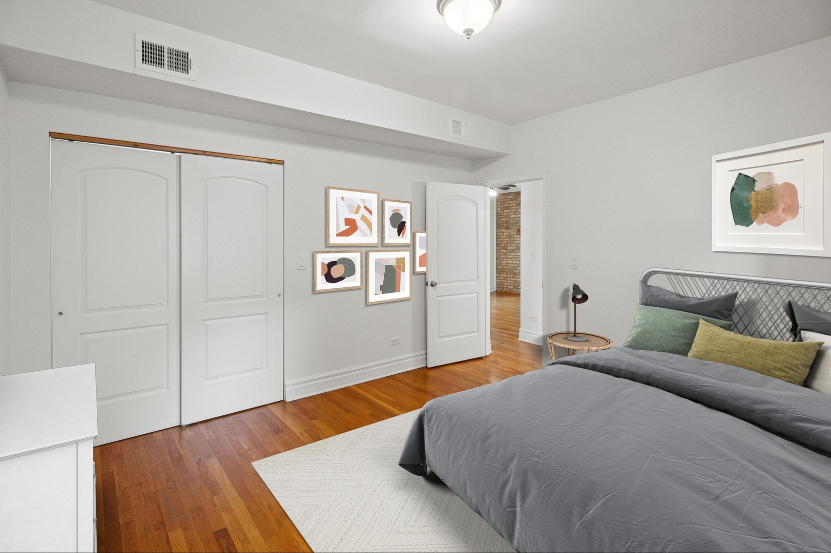 Bedroom with a gray bed, green accent pillows, hardwood floors, and white closet doors.
