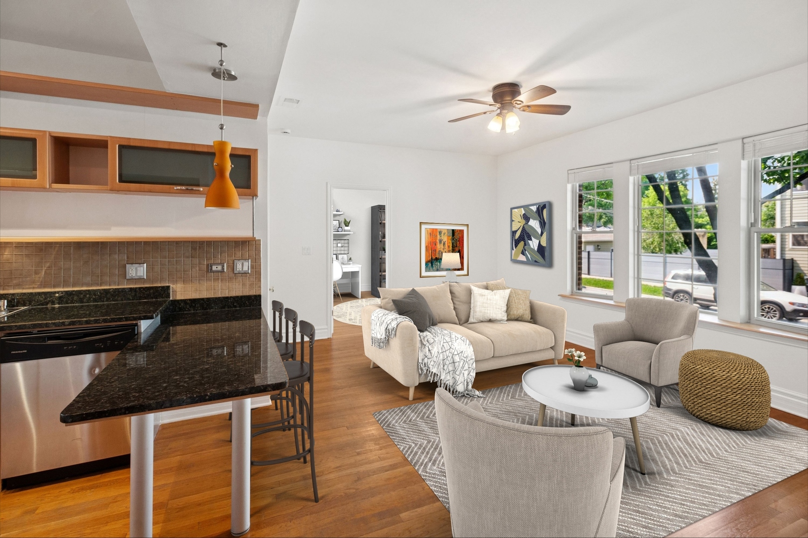 Open-plan living room and kitchen with a granite breakfast bar, hardwood floors, and large windows.