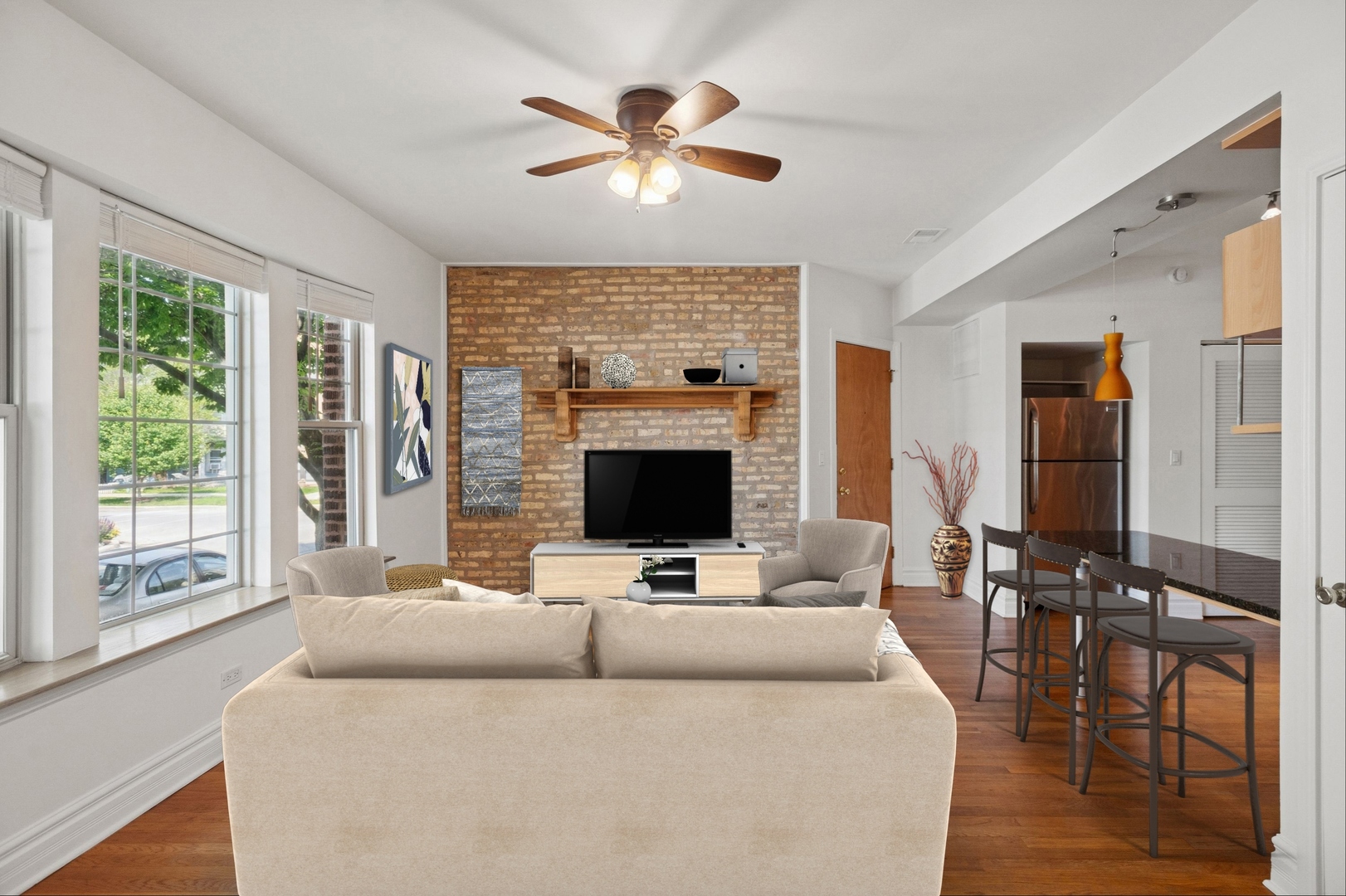 Living room with a brick accent wall, large windows, and an open kitchen with bar seating.