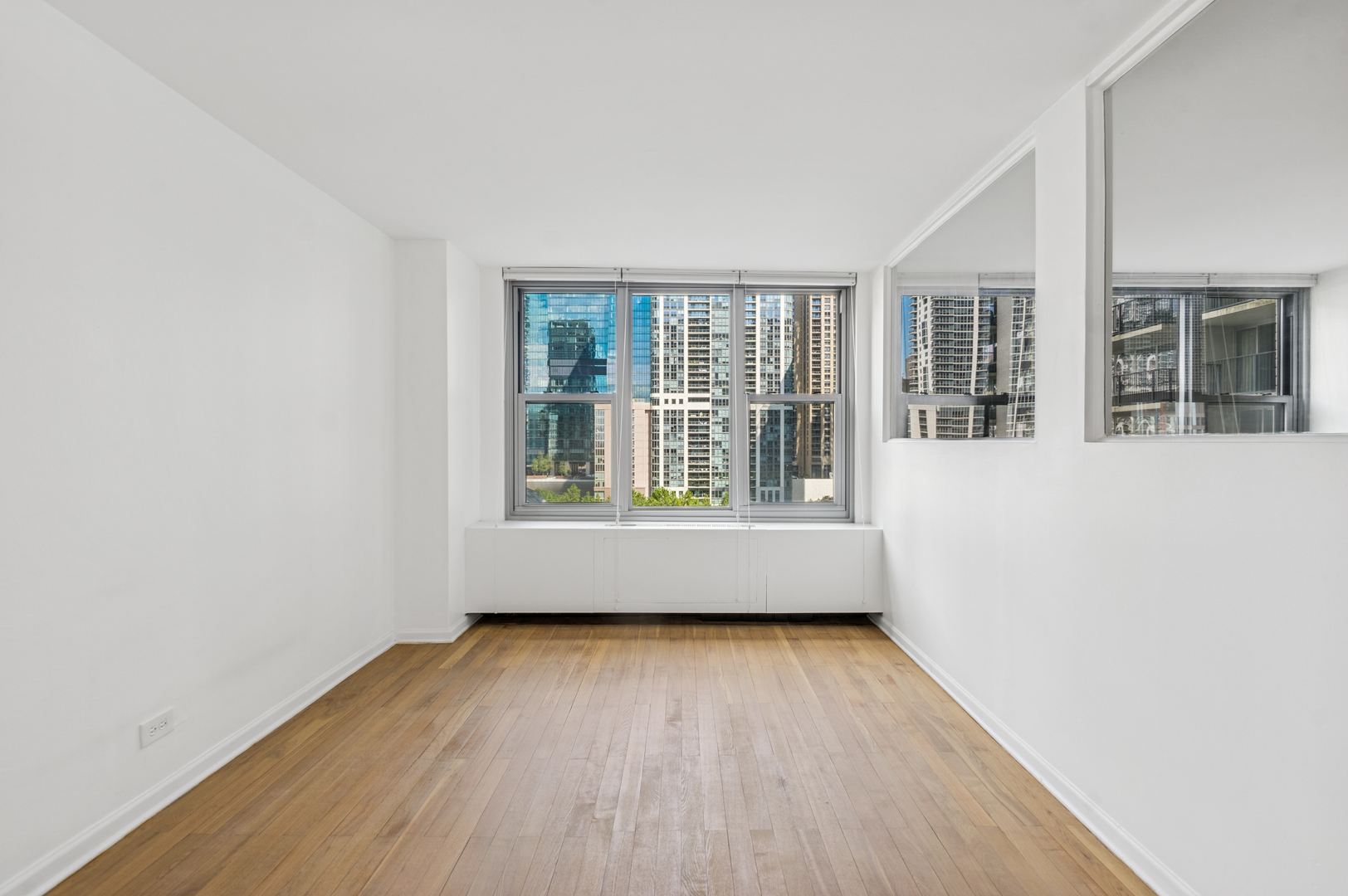 Empty room with hardwood floors, large windows, and views of downtown buildings.