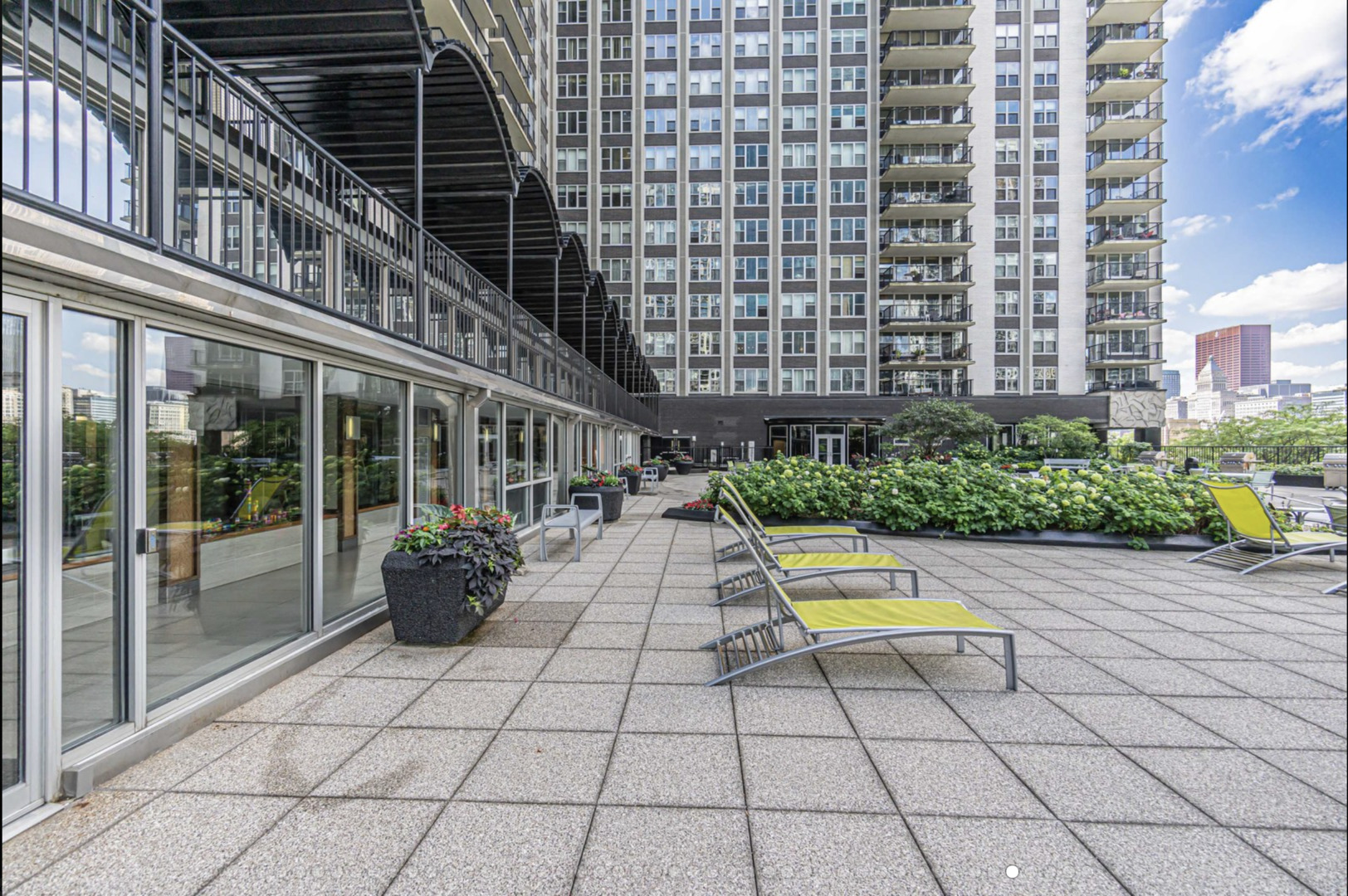 Condominium terrace with yellow lounge chairs, landscaped planters, and high-rise buildings.