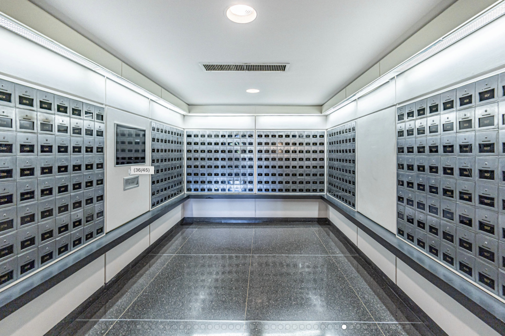 Building mailroom with rows of metal mailboxes and a dark tiled floor.