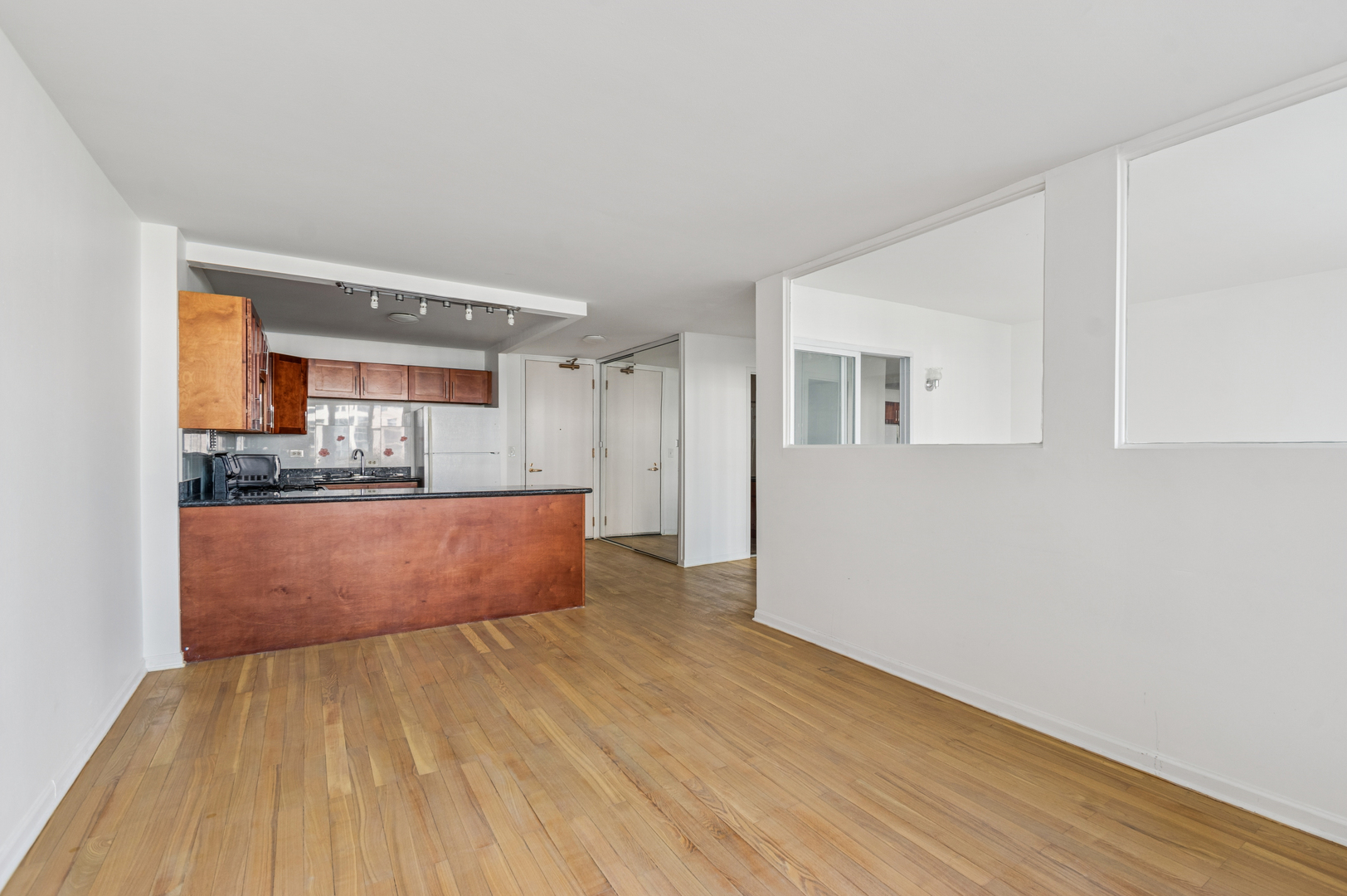 Vacant condo living area with hardwood floors and an open kitchen with wood cabinets and a breakfast bar.