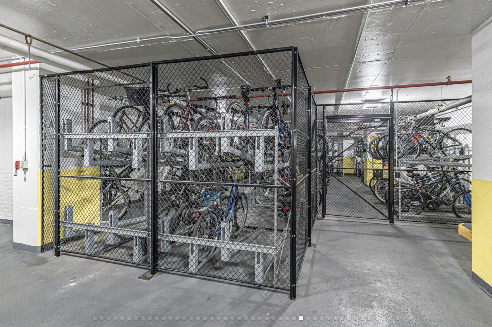 Secured indoor bicycle storage room with rows of bikes on racks behind chain-link fencing.
