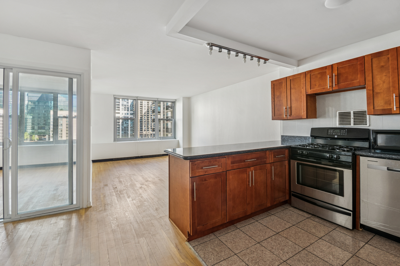Unfurnished condo kitchen with a wood-cabinet island, stainless steel range, and windows overlooking high-rises.