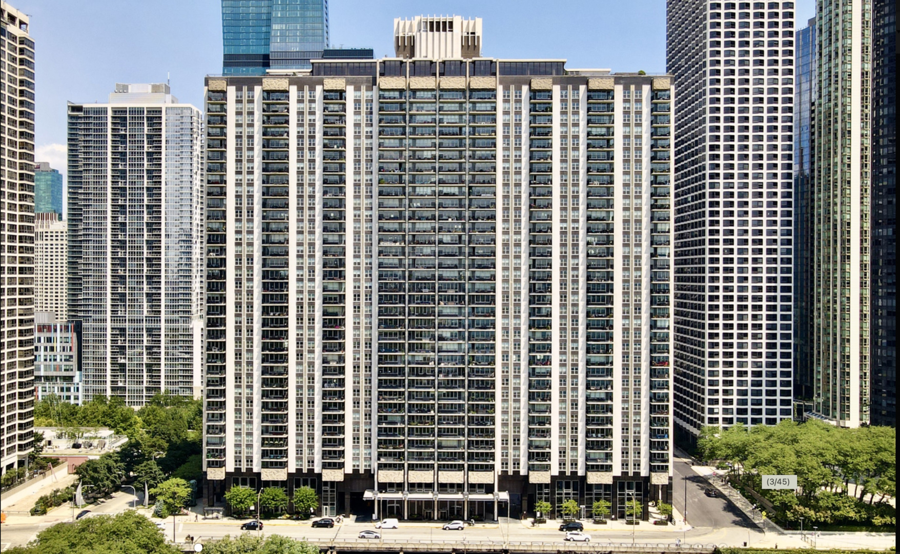 Chicago residential high-rise with rows of balconies, framed by downtown towers and leafy trees.