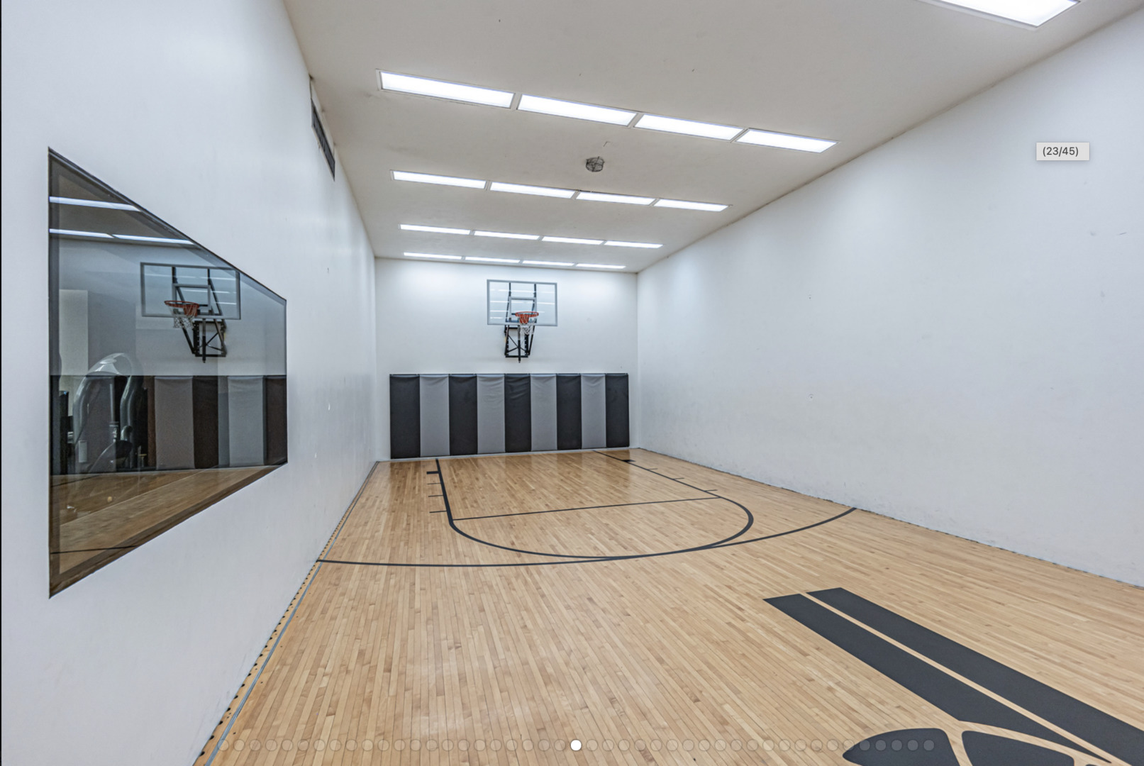 Indoor basketball court with a polished hardwood floor, two hoops, and a glass viewing window.
