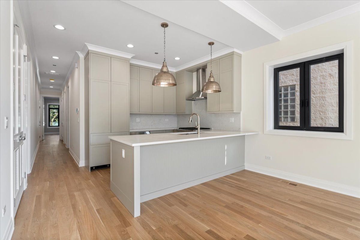 Unfurnished kitchen with a large island, light cabinetry, pendant lights, and hardwood floors.