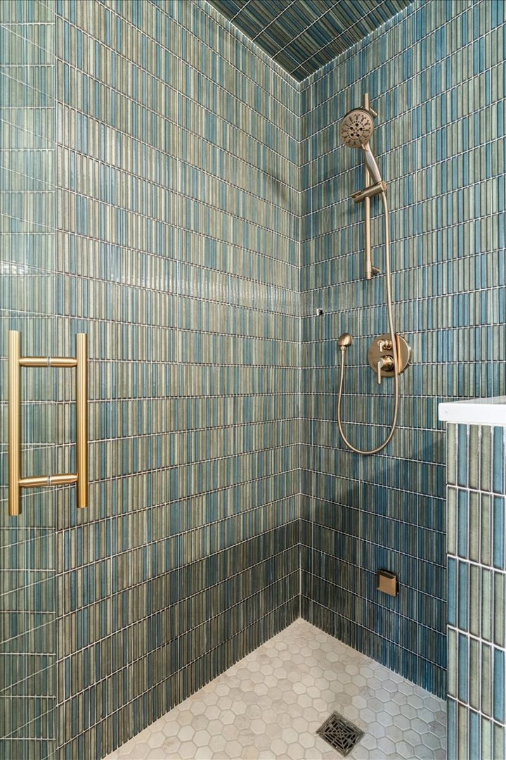 Walk-in shower with blue-green tile, brass fixtures, and a light hexagonal tile floor.