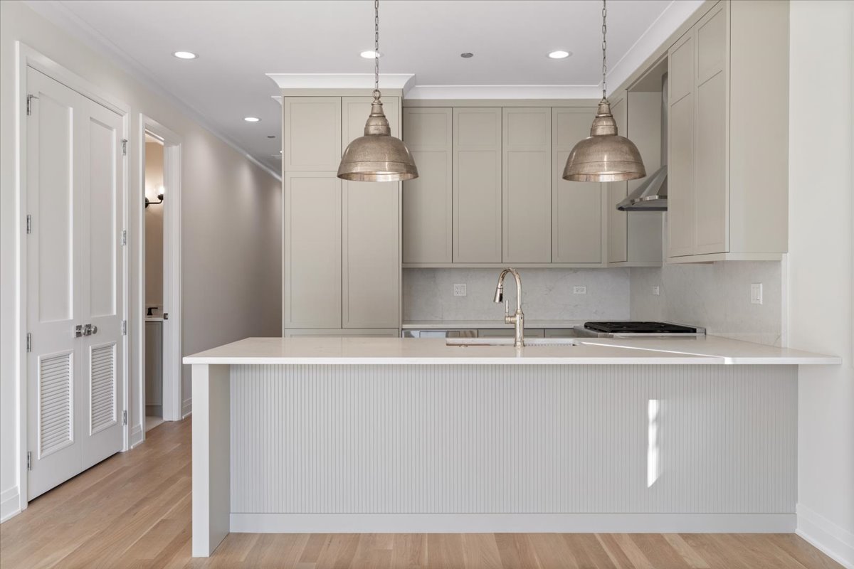 Modern kitchen with pale cabinetry, a large fluted island, and two metal pendant lights.