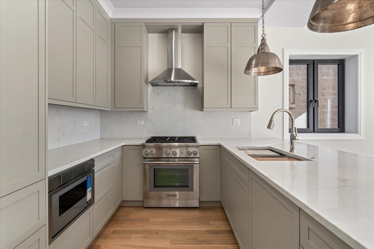 Modern U-shaped kitchen with gray shaker cabinets, marble-look counters, stainless appliances, and wood flooring.