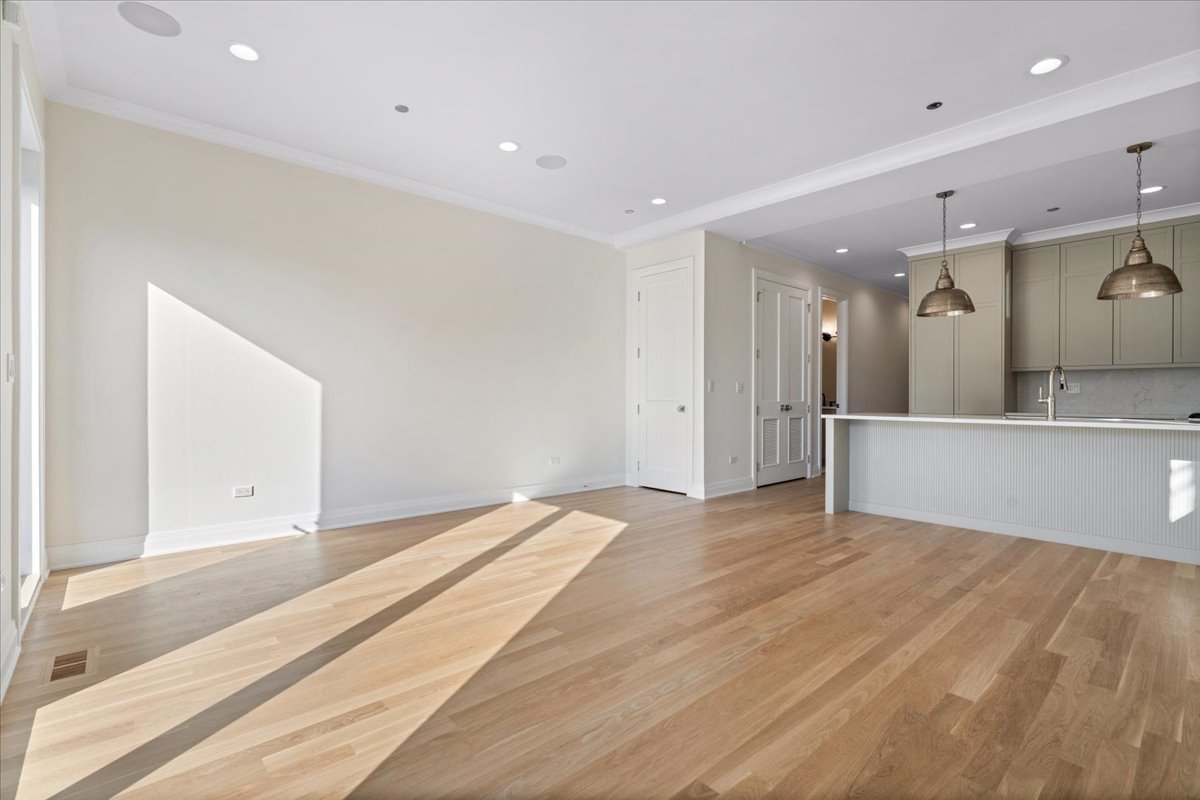 Bright vacant living area with oak floors and an open kitchen with a white peninsula.