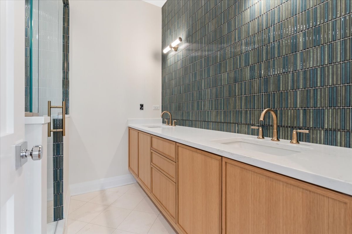 Bathroom with a double vanity, light wood cabinets, and dark teal tiled wall.