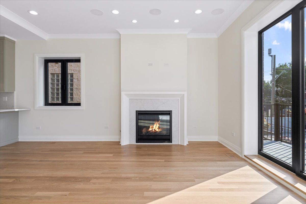 Vacant living room with a marble-surround fireplace, oak floors, and black-framed balcony doors.