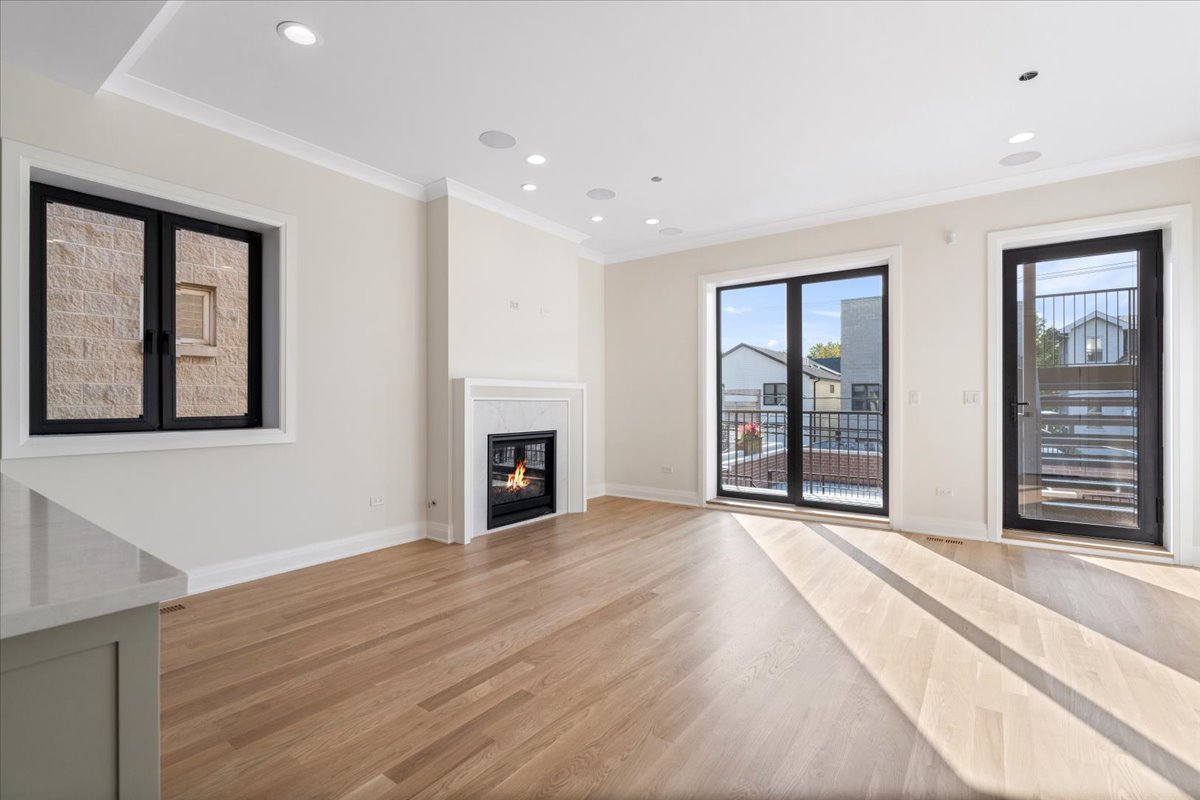 Vacant living room with hardwood floors, a gas fireplace, and doors to a balcony.