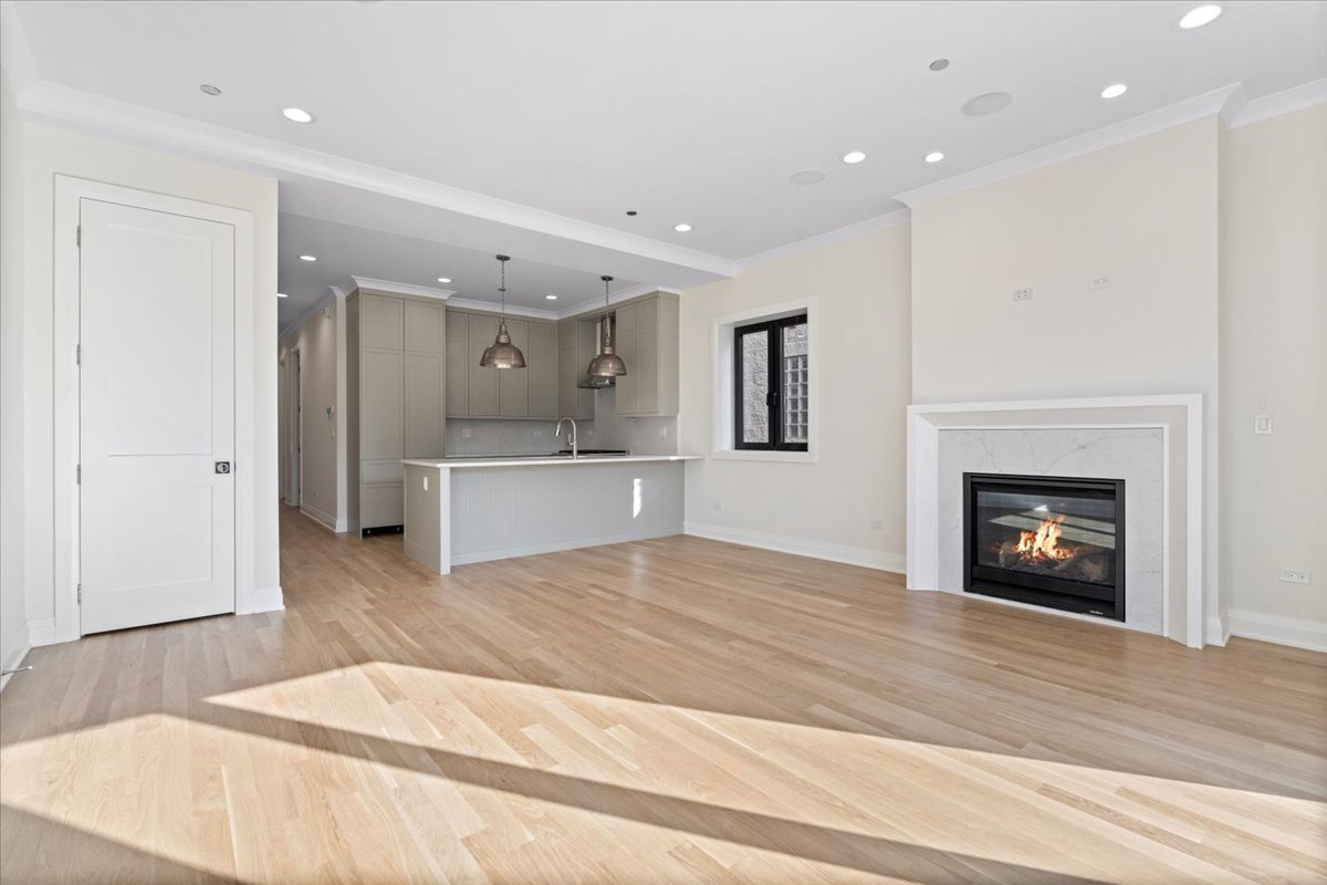 Open living room and kitchen with hardwood floors, a white island, and a gas fireplace.
