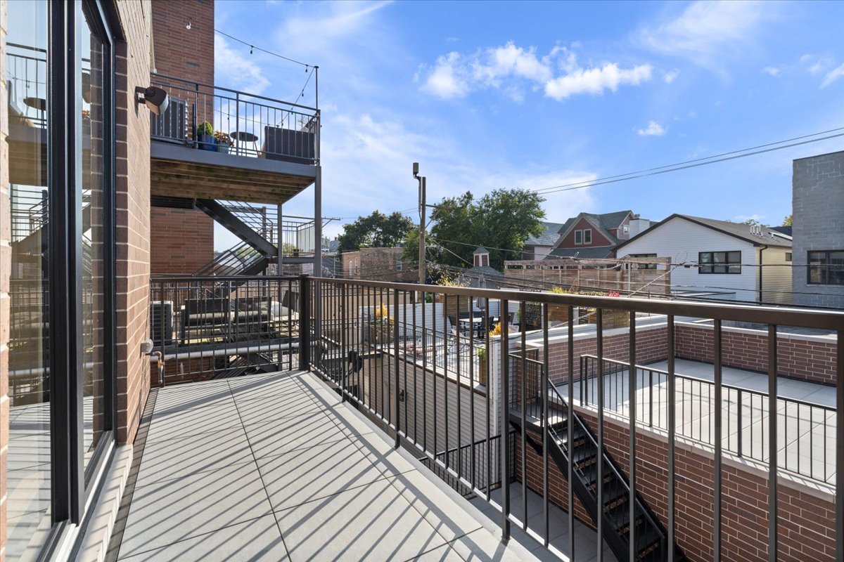 Elevated balcony with gray decking, black metal railings, and views of neighboring rooftops.