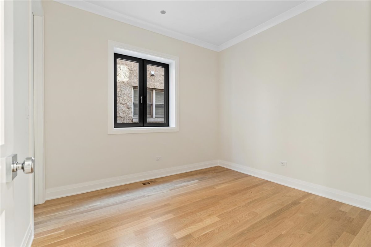 Empty bedroom with hardwood floors and a black-framed window.