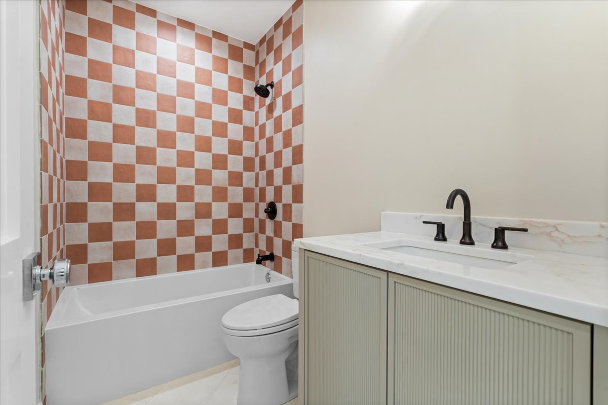 Bathroom with terracotta-and-white checkerboard shower tile, a bathtub, and a pale vanity with black fixtures.