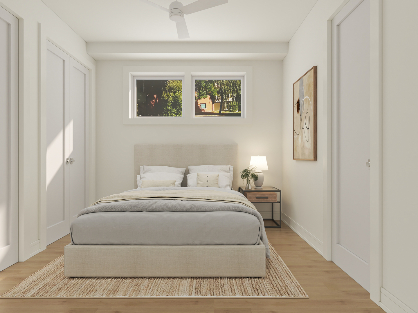 Staged bedroom with a neutral upholstered bed beneath two high windows overlooking leafy trees.