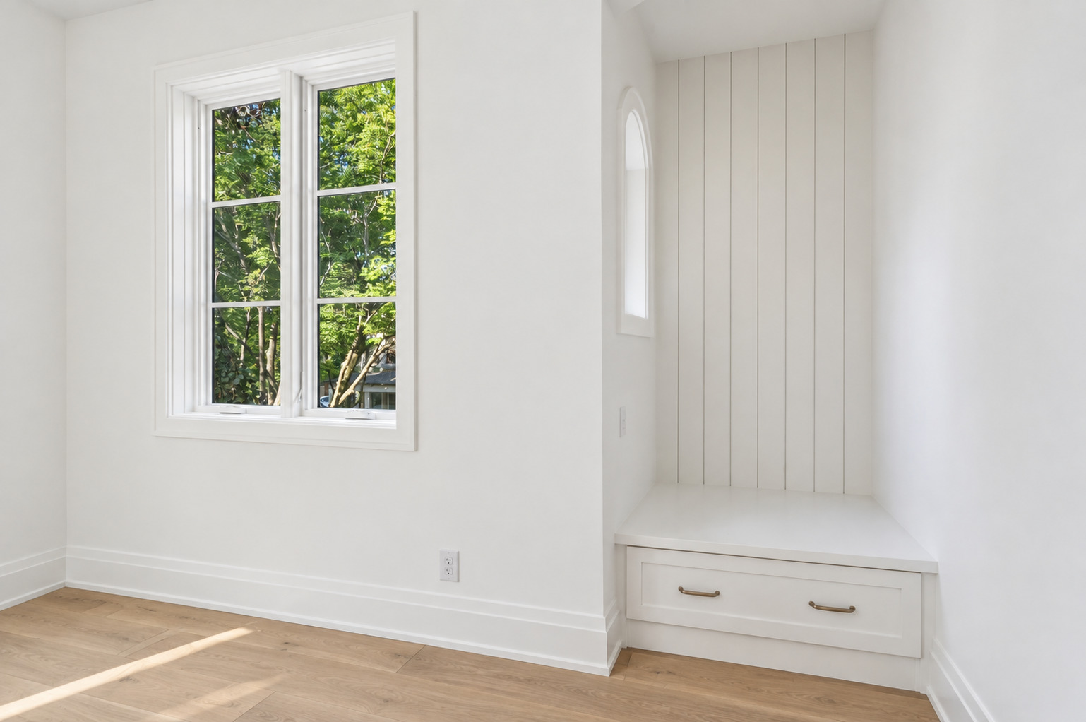 Bright room with a leafy view through a tall window and a built-in paneled window seat.
