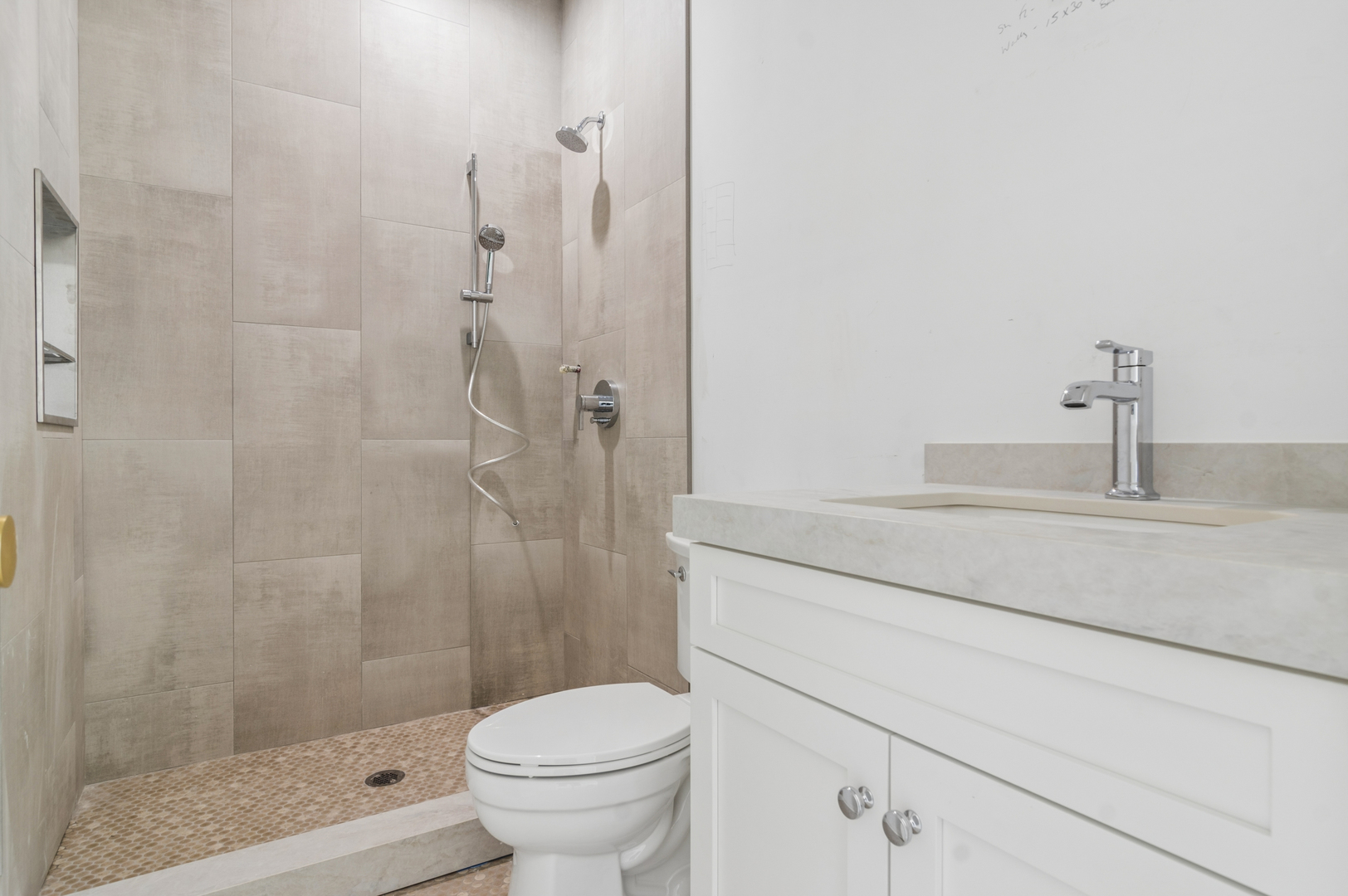 Modern bathroom with a beige tiled walk-in shower, white vanity, and toilet.