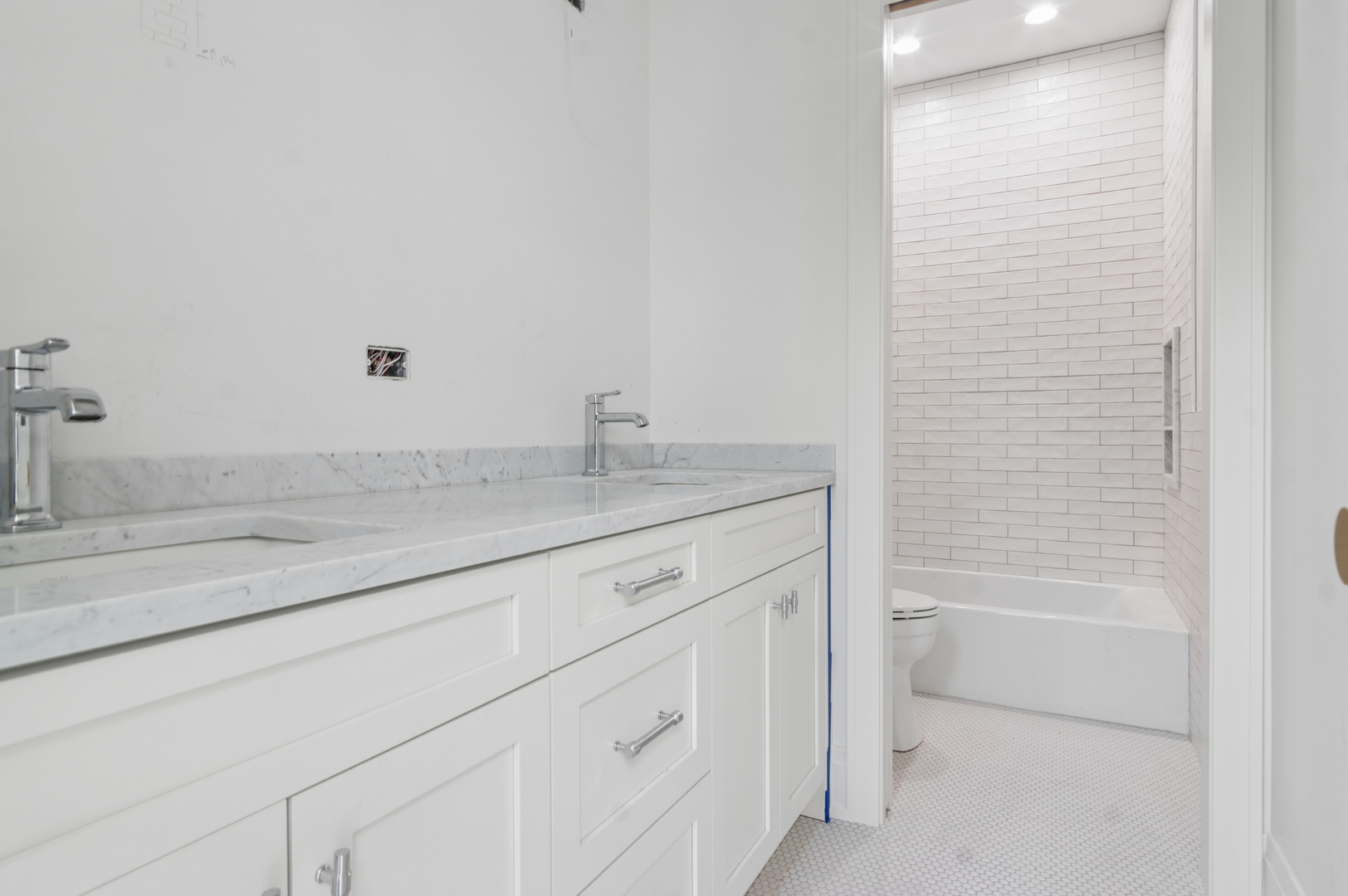 Bathroom with marble double vanity and white subway-tile tub surround.