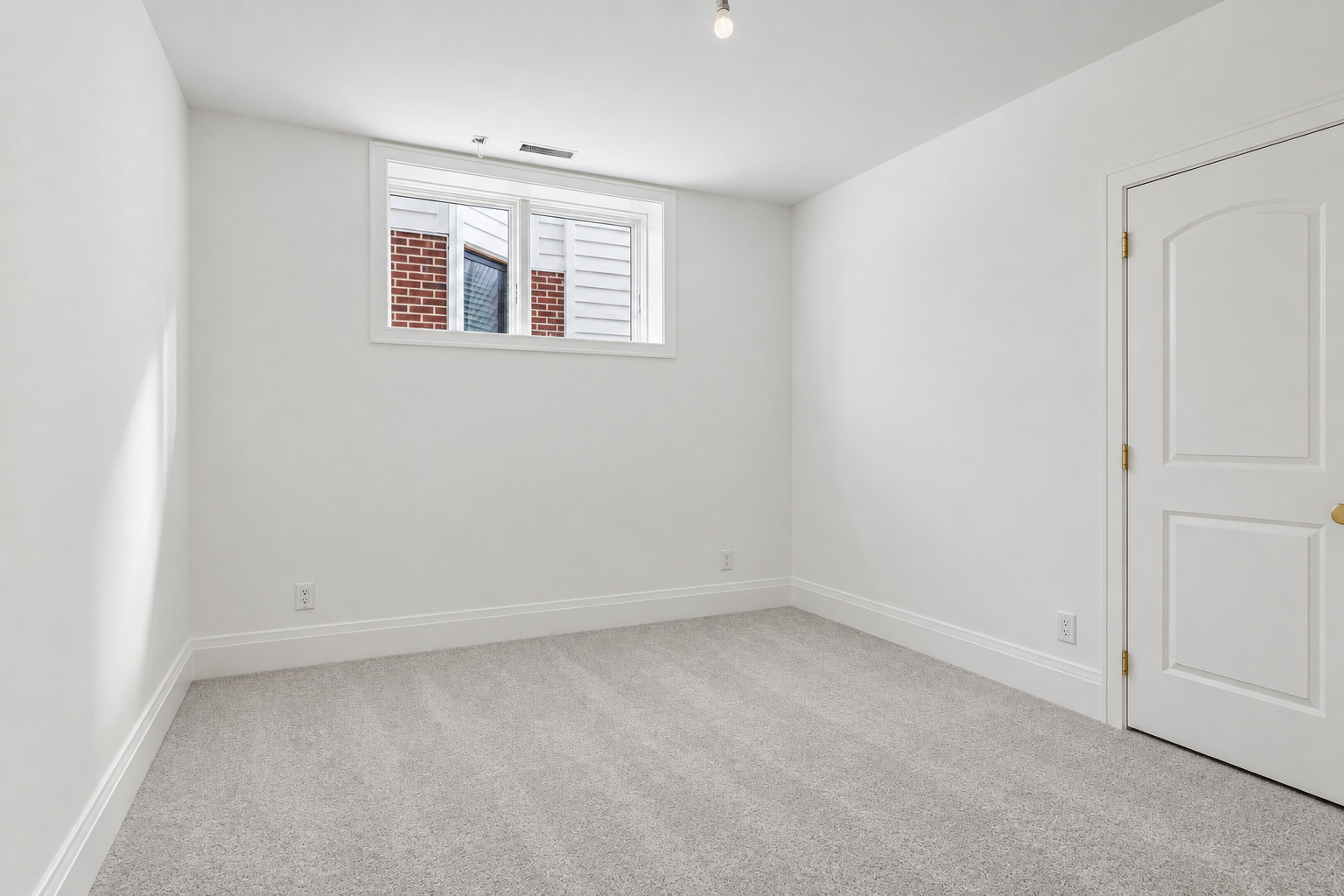 Empty carpeted room with white walls, a high-set window, and a paneled door.