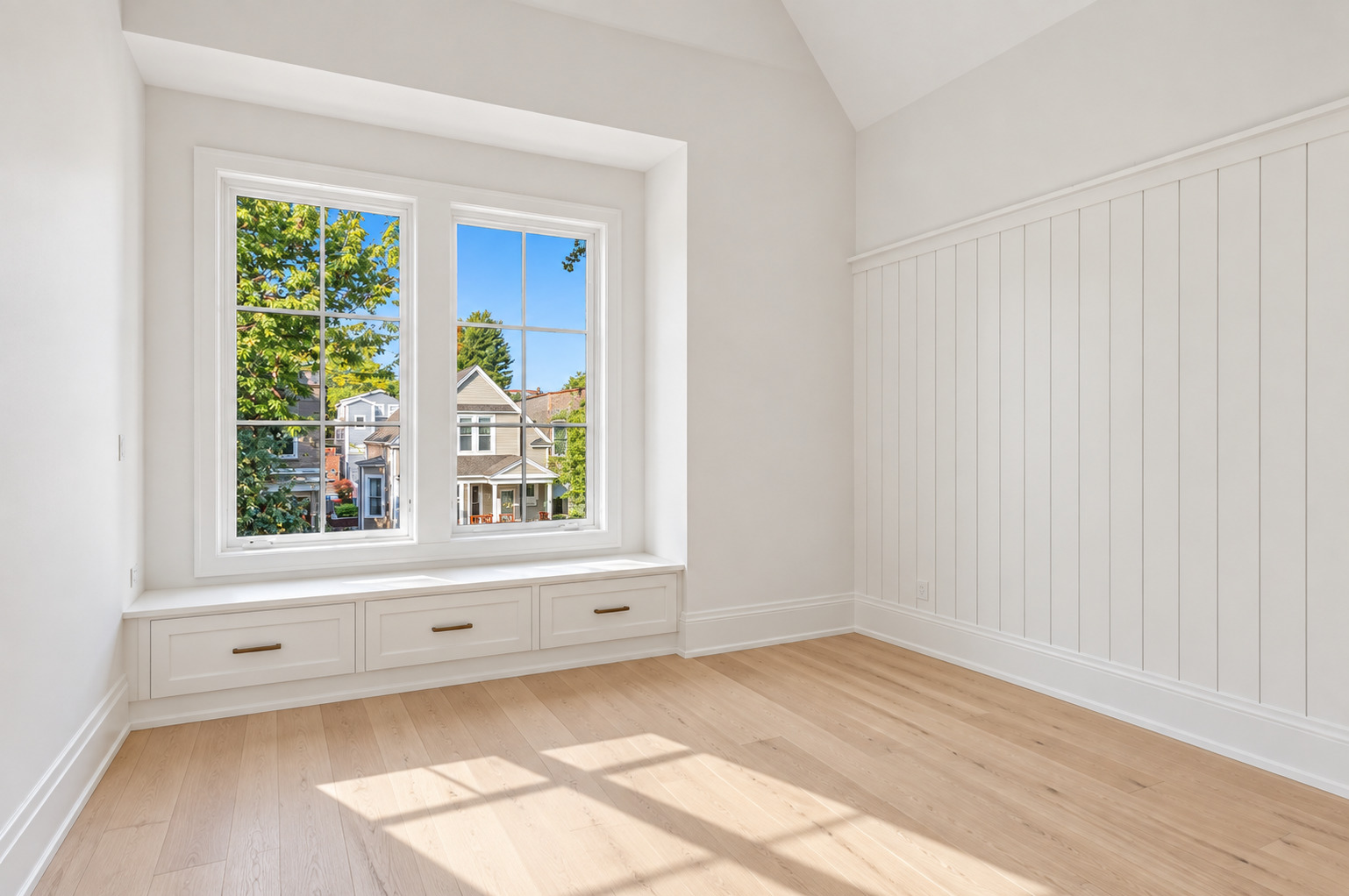 Bright empty room with a built-in window seat, drawer storage, and sunlight on pale wood floors.