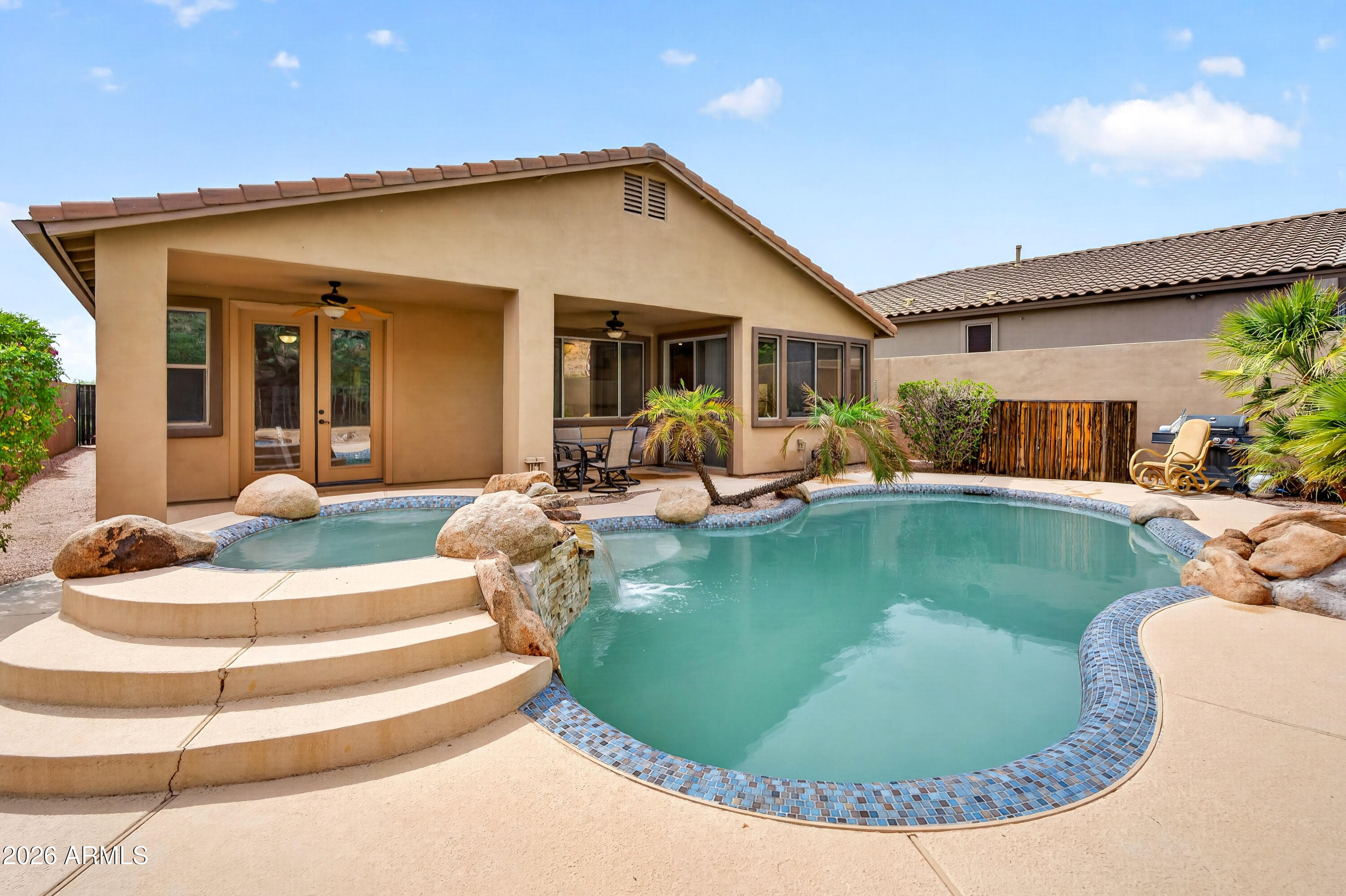 Backyard pool with curved blue-tile edging, wide steps, and a covered patio beside a tan stucco home.