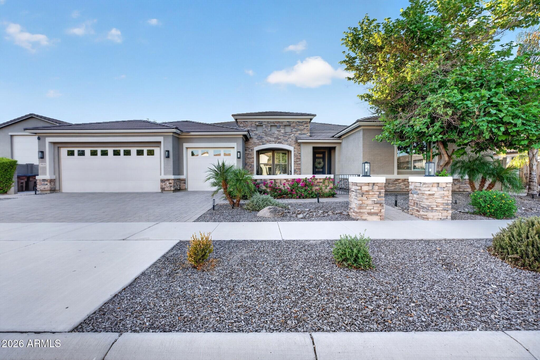 Single-story gray home with stone accents, two garage doors, and desert landscaping.