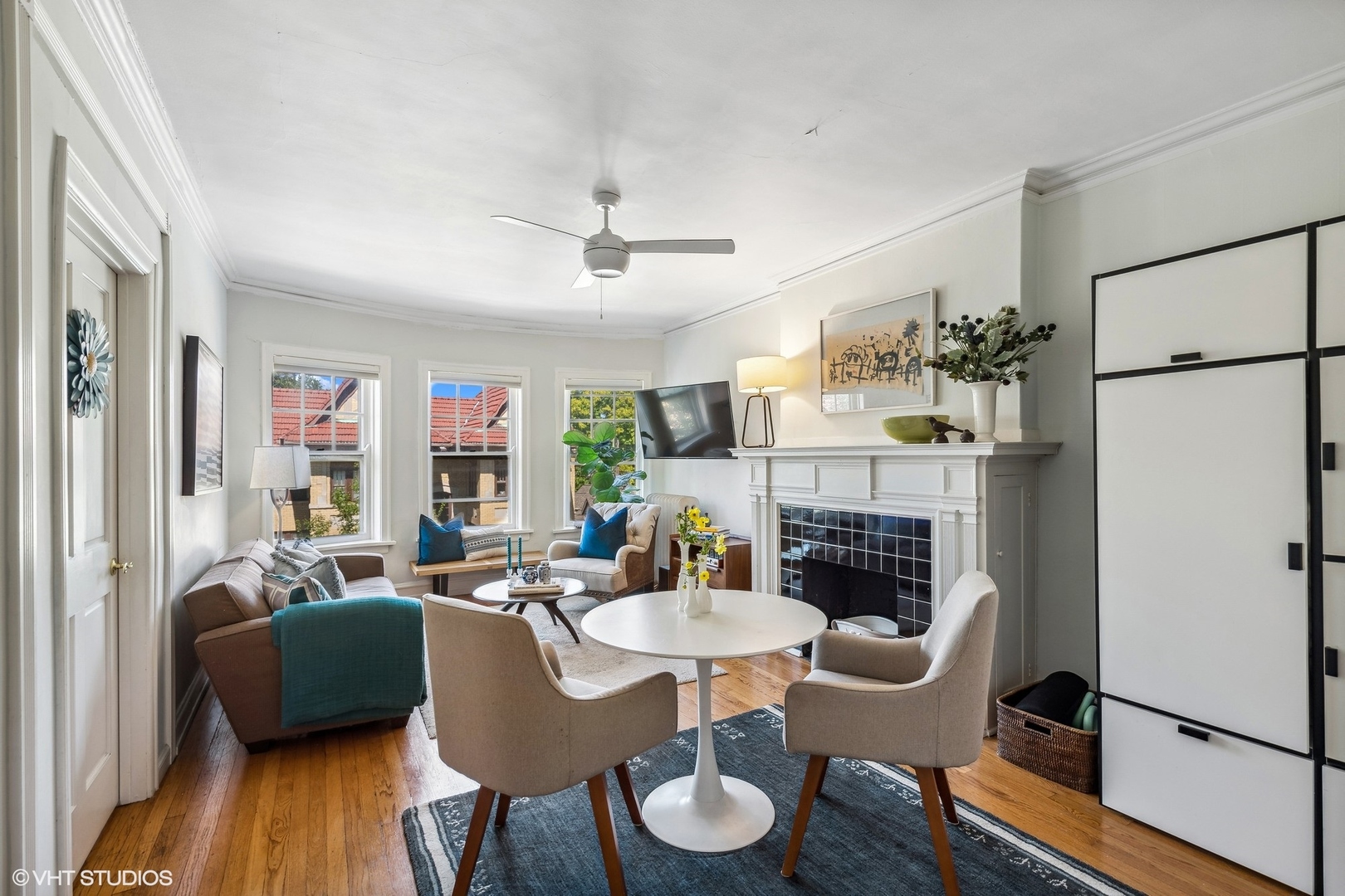 Furnished living room with a tiled fireplace, tall windows, hardwood floors, and a round table with chairs.