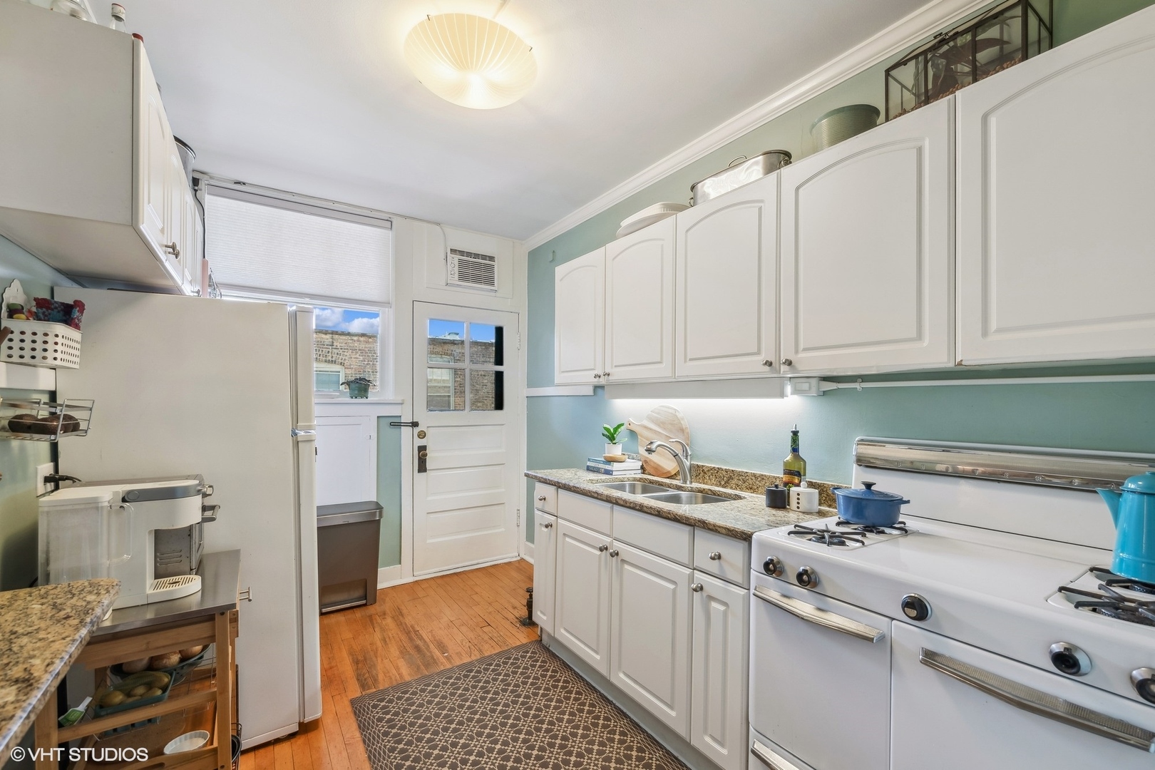 Kitchen with white cabinets and appliances, granite counters, and warm wood floors.