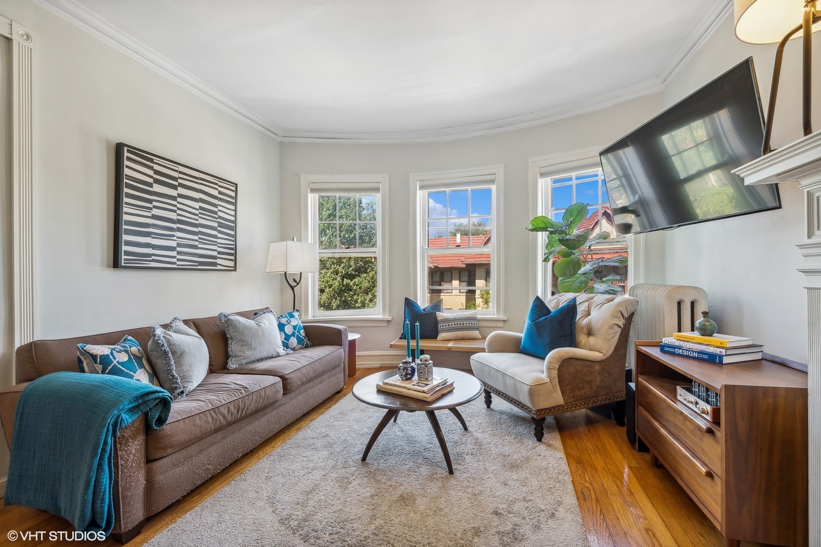Bright living room with a brown sofa, cream armchair, and three windows.