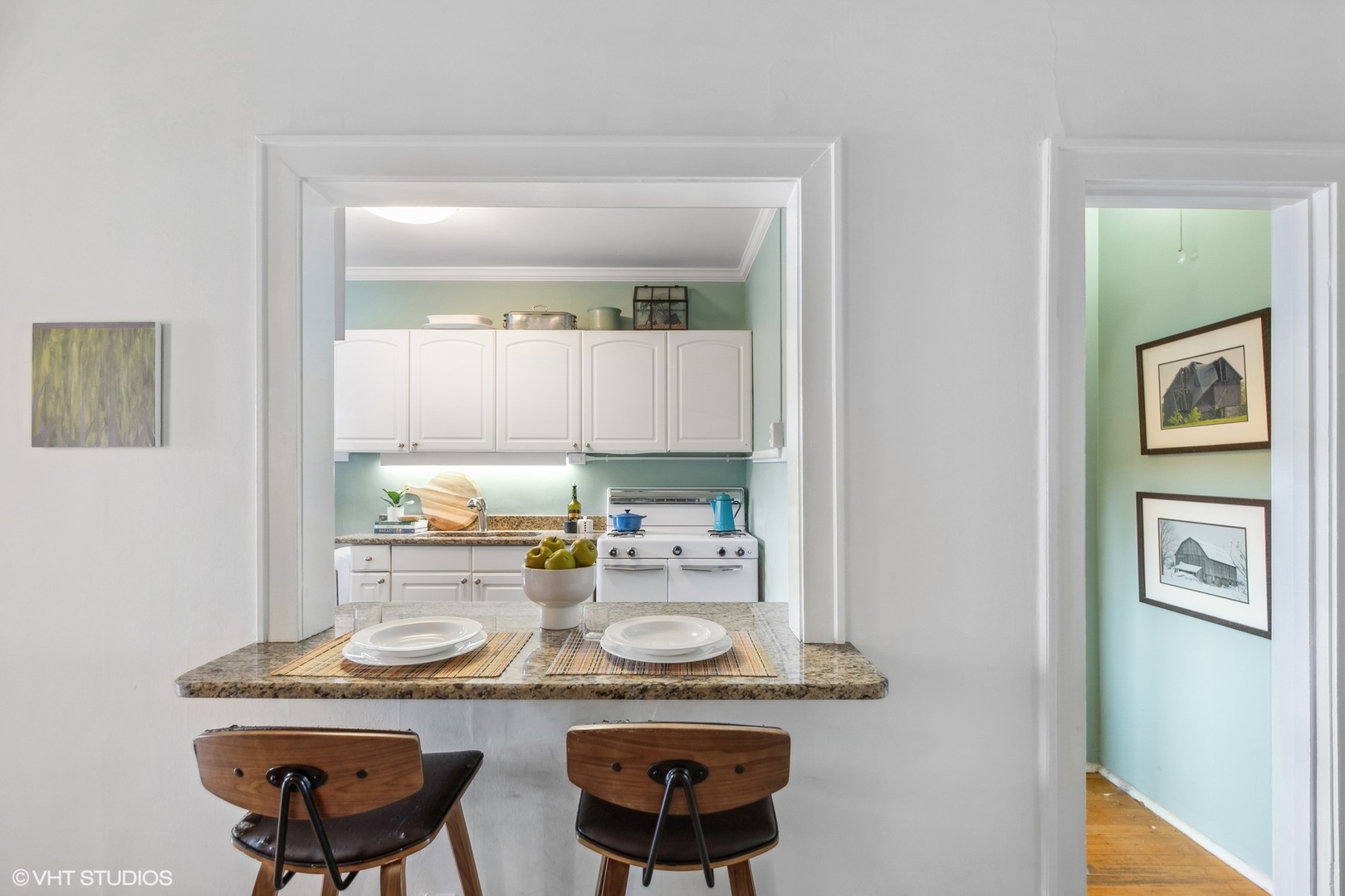 Kitchen with white cabinets, granite breakfast bar set for two, and mint-green hallway.