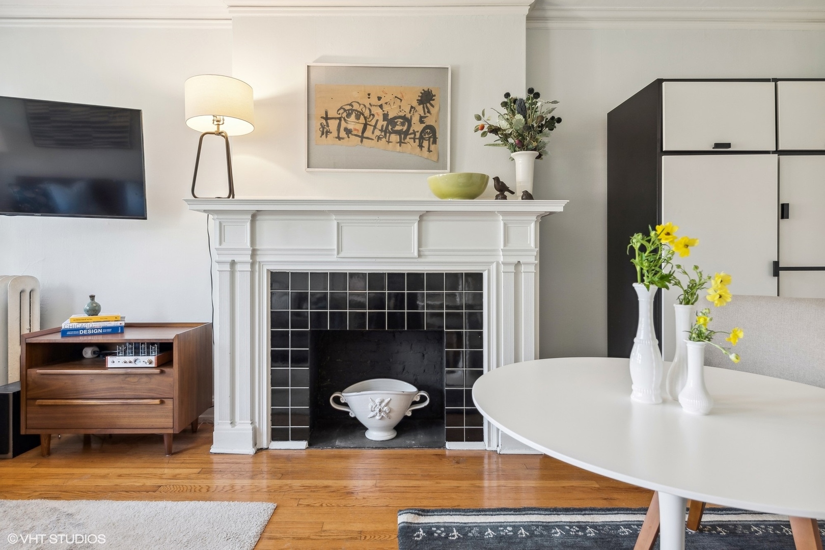 Living and dining area with a black-tiled fireplace, white mantel, and hardwood floors.