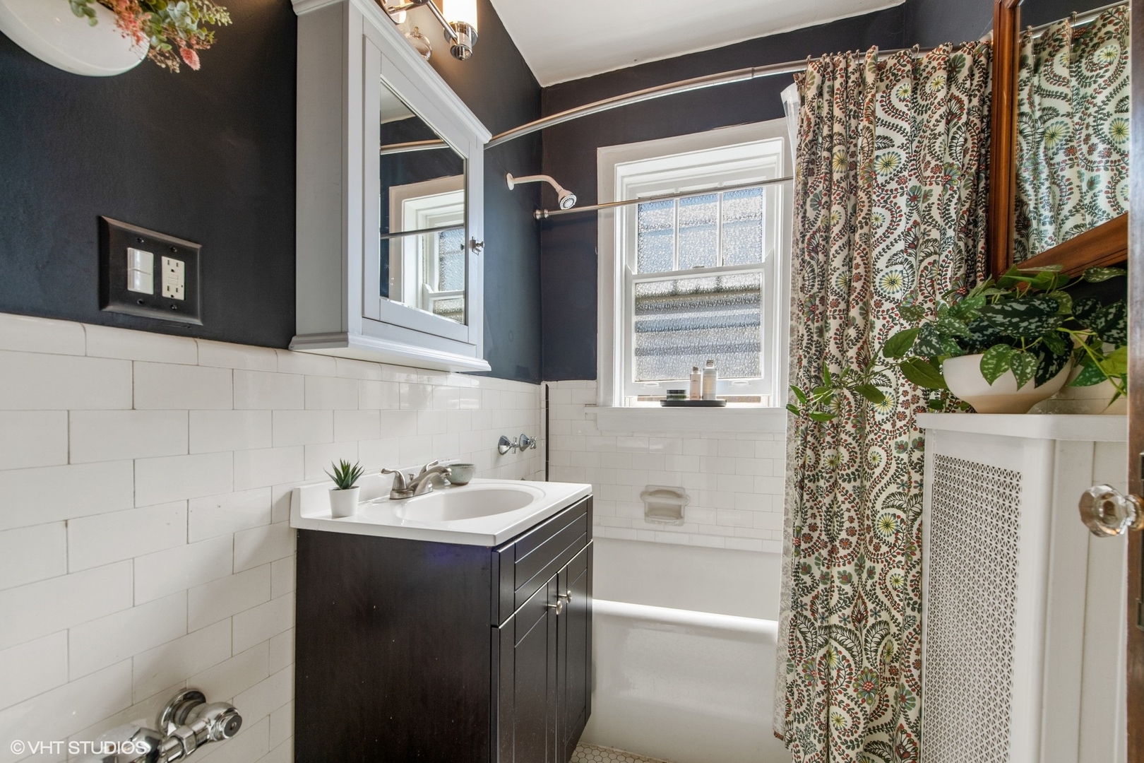 Bathroom with a dark vanity, white subway tile, and a patterned shower curtain beside the tub.