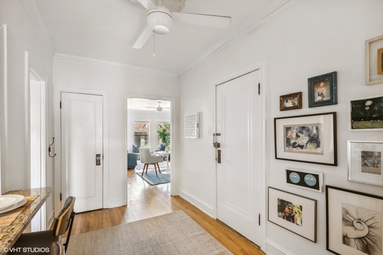 Apartment entry hall with hardwood floors, white paneled doors, and a gallery wall of framed art.