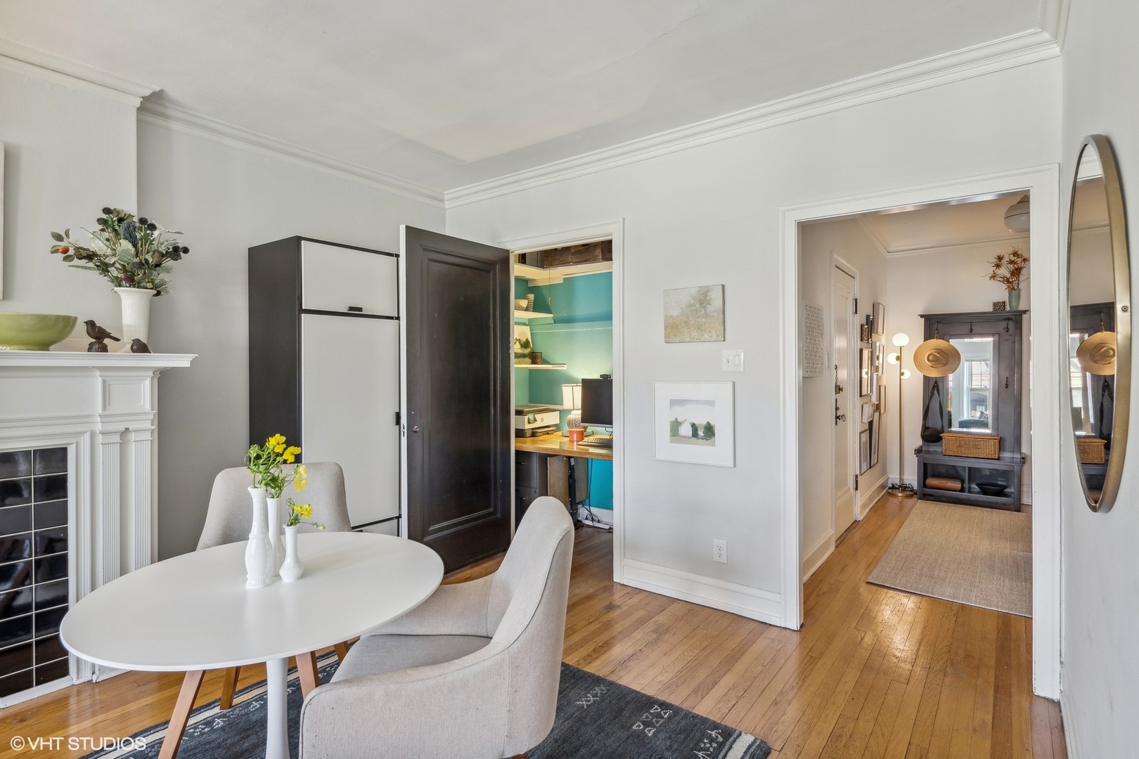 Dining area with a white oval table beside a fireplace, opening to a turquoise office nook and hallway.