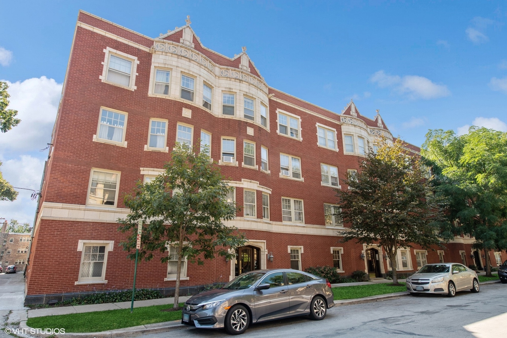 Red-brick apartment building with ornate stone trim and trees along the sidewalk.