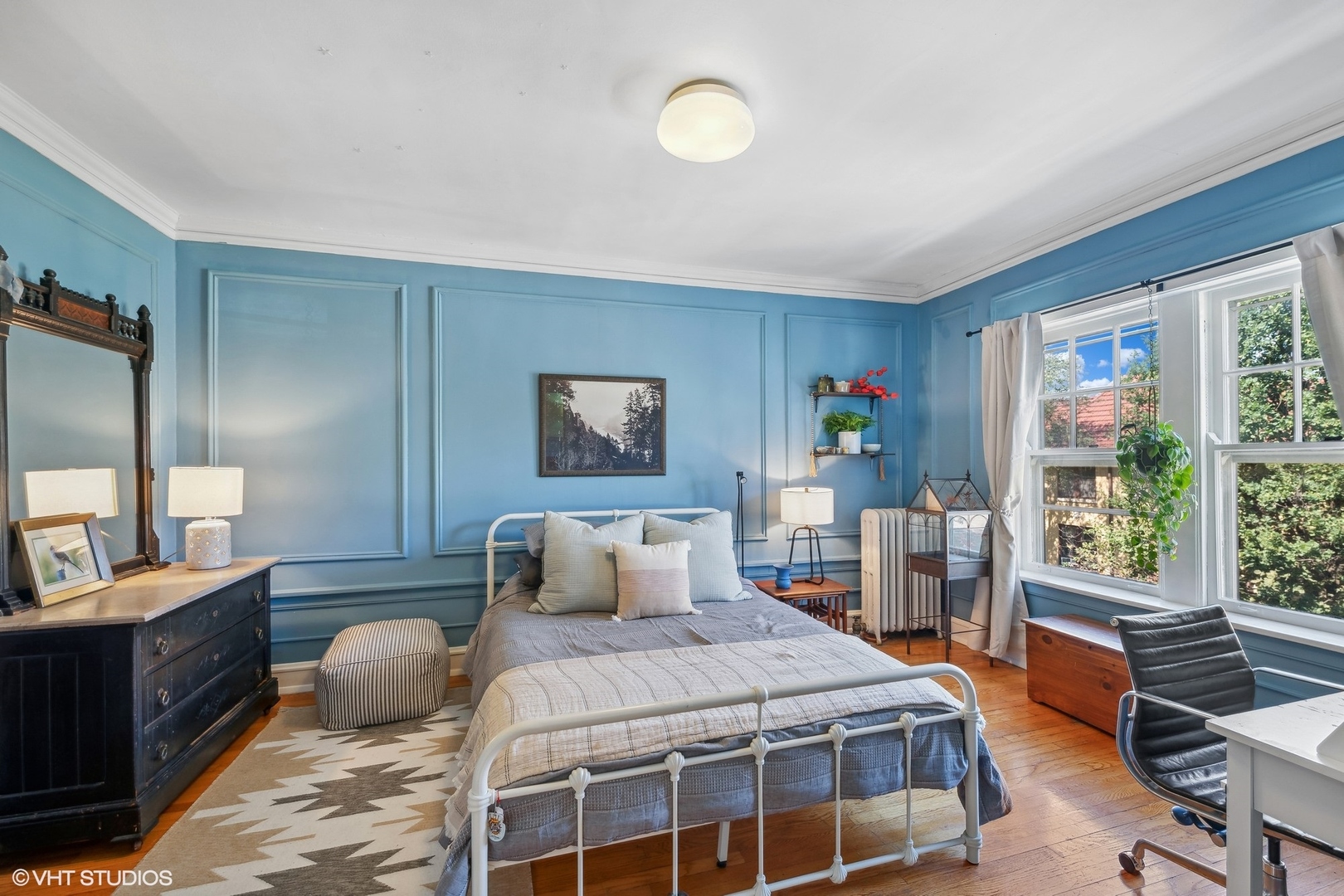 Blue bedroom with paneled walls, a white metal bed, and large sunny windows.