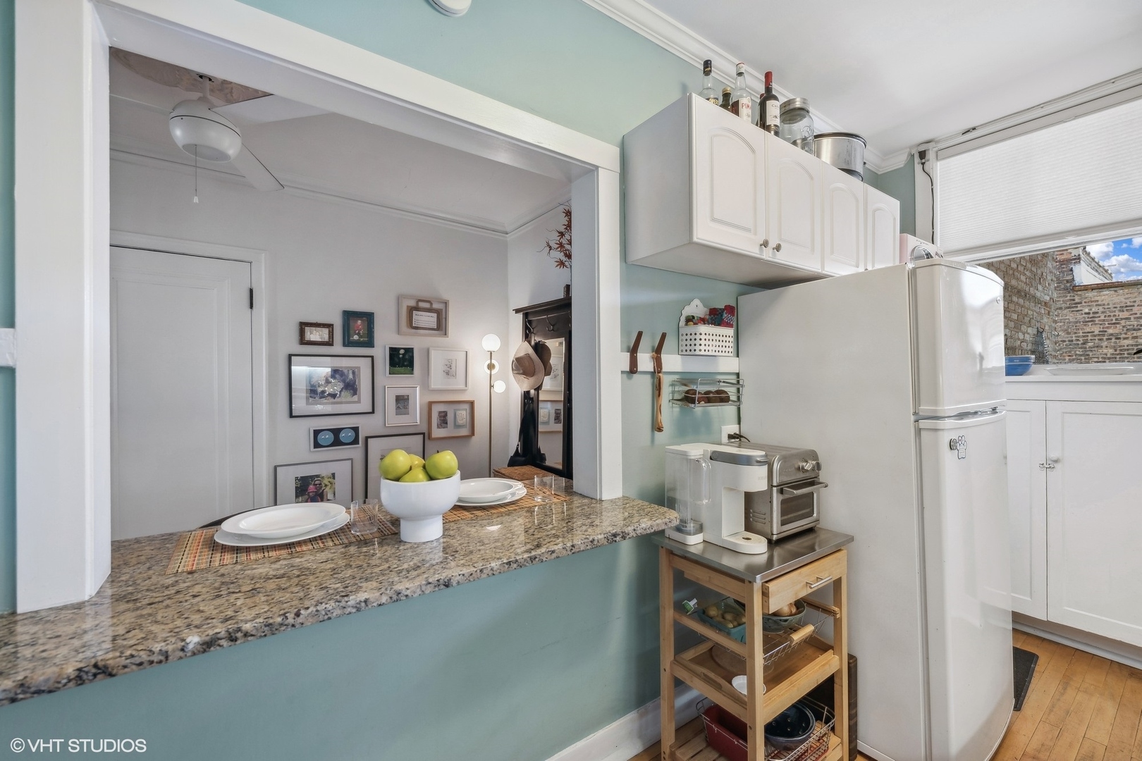Kitchen with aqua walls, white cabinets, and a granite pass-through counter topped with plates and green apples.