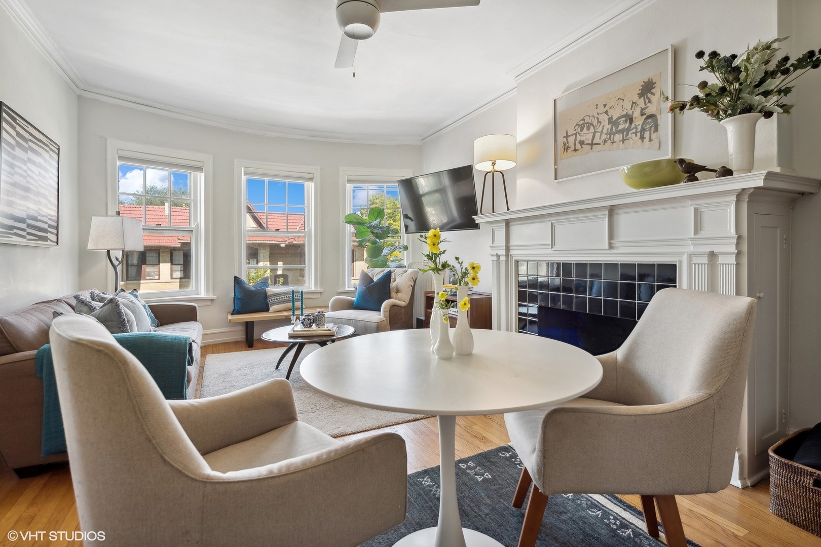 Living room with a white fireplace, three tall windows, and neutral seating.