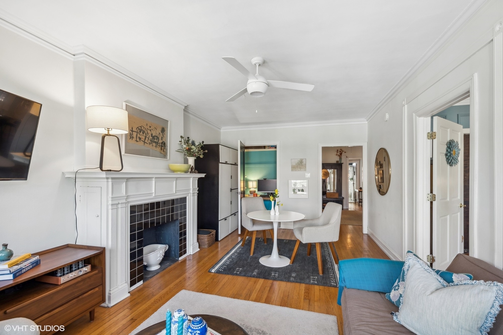 Living room with a white fireplace, hardwood floors, and a round table between two chairs.