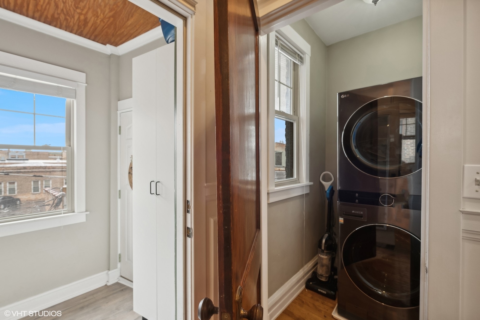 Laundry area with a stacked washer and dryer beside windows and white built-in cabinets.