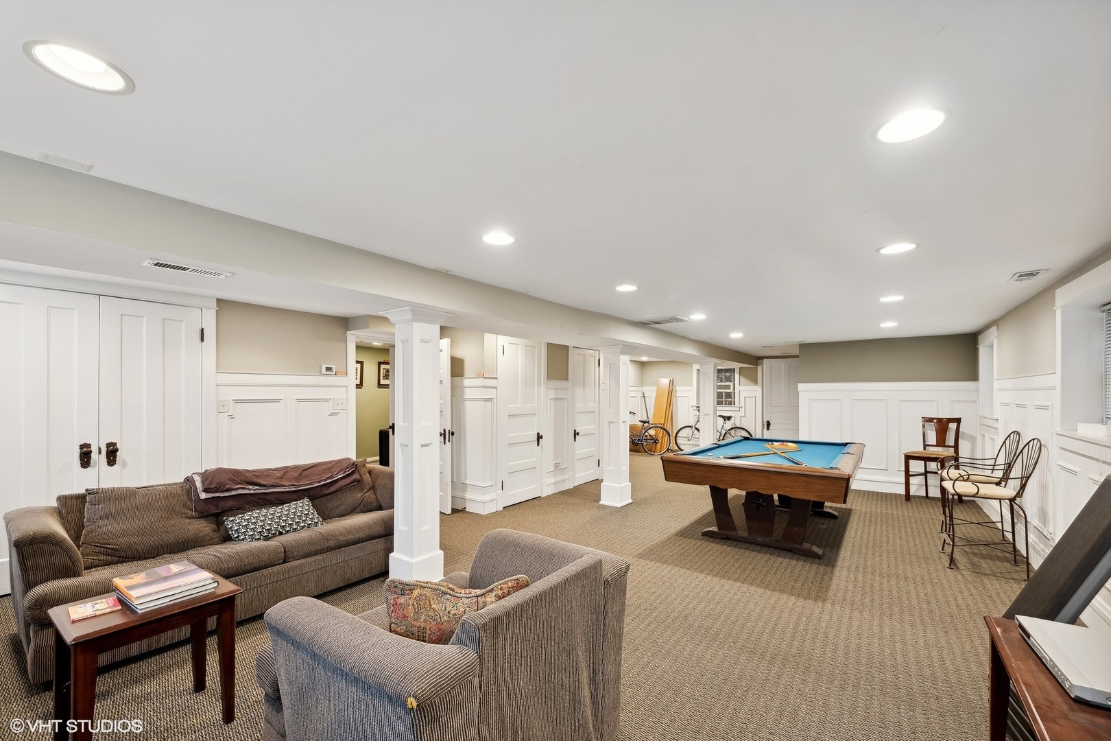 Basement recreation room with a pool table, sofas, and bicycles along the back wall.