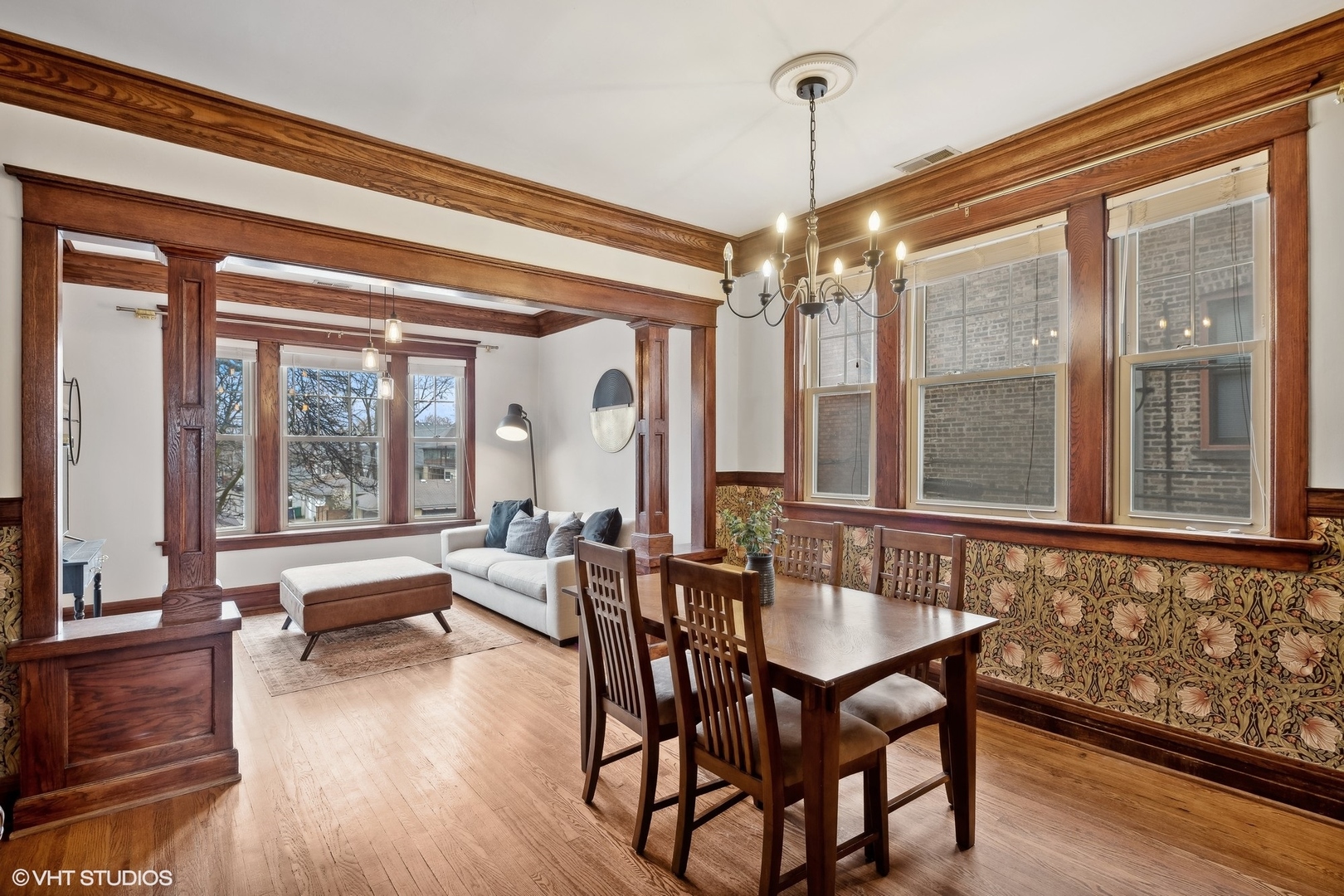Living and dining room with ornate wood trim, hardwood floors, and large windows.