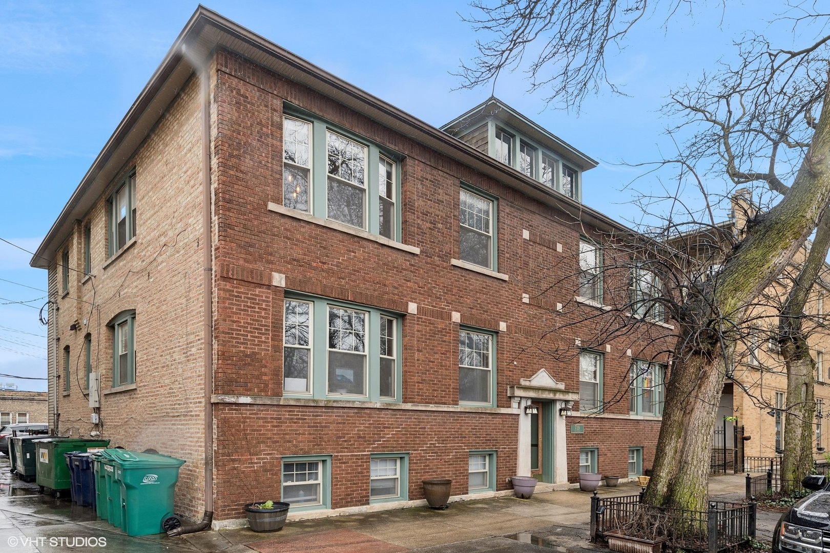 Brick apartment building with pale green trim, recessed entrance, and a large leafless tree.