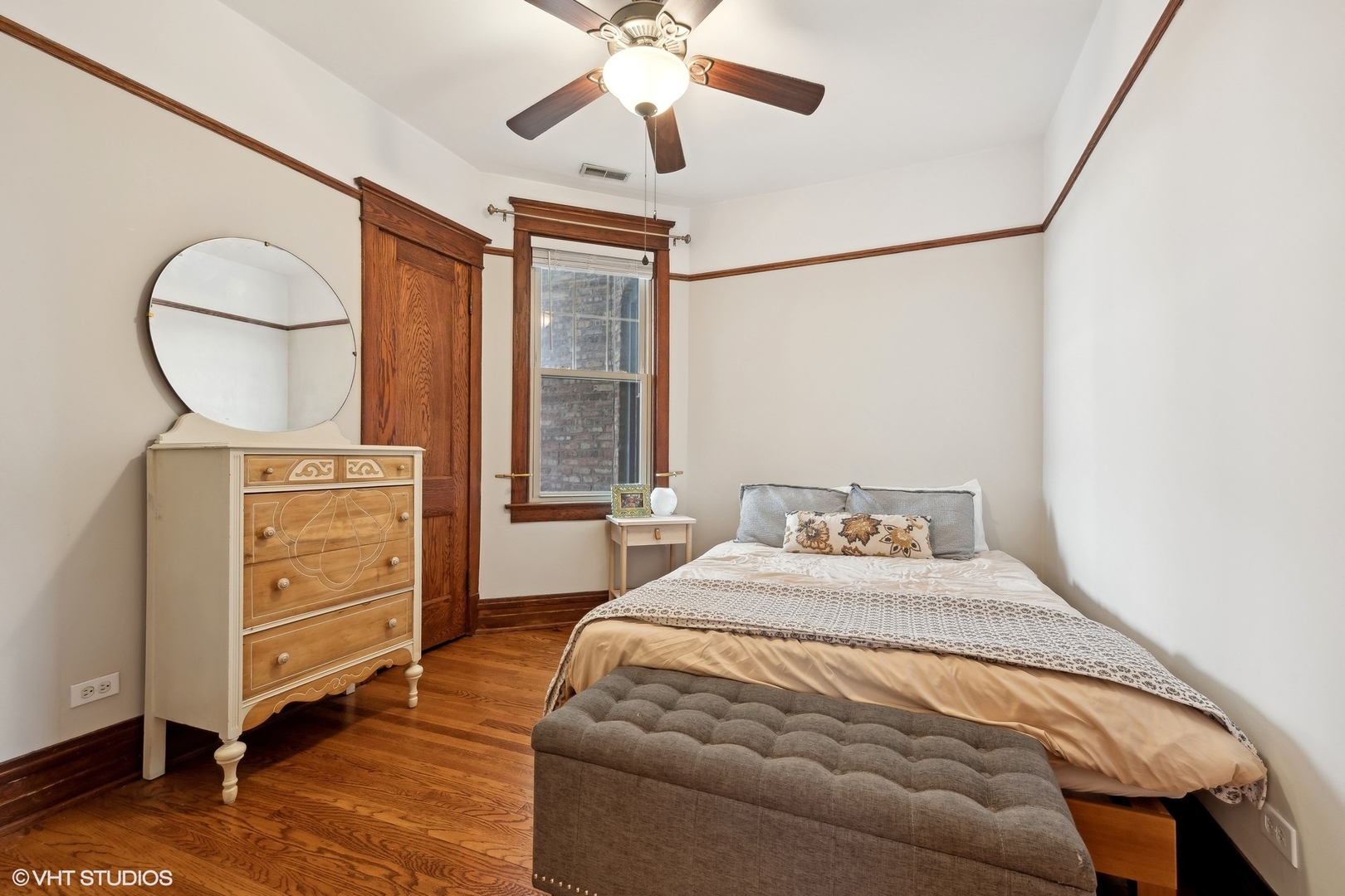 Bedroom with hardwood floors, ornate wood trim, and a bed beneath a ceiling fan.